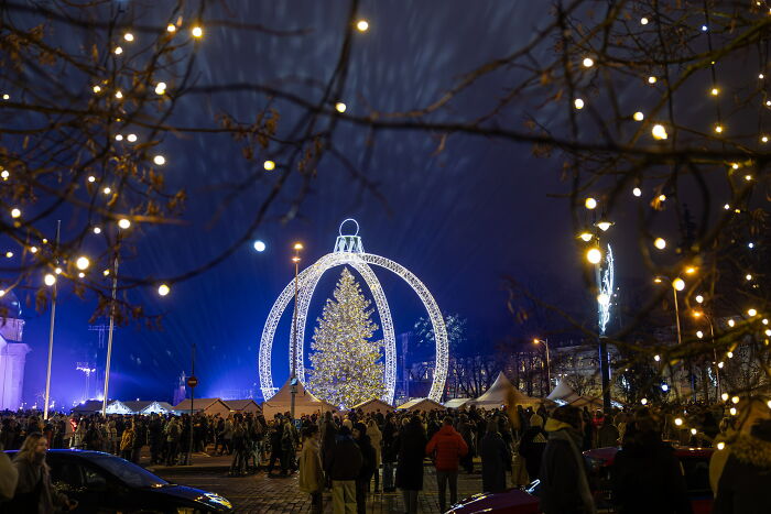 Illuminated Vilnius Christmas tree in a city center with festive lights and a crowd of people gathered around.