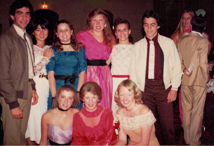 Group of high school students from the '70s dressed in colorful formal attire at a dance or prom event.