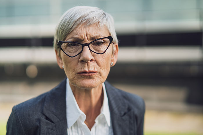 Angry woman in a shopping mall, wearing glasses and a blazer, expressing frustration and demanding a seat.