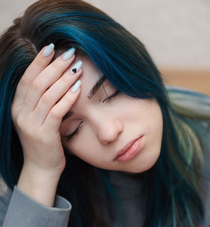 Tired woman with blue hair holding her head in a shopping mall. 