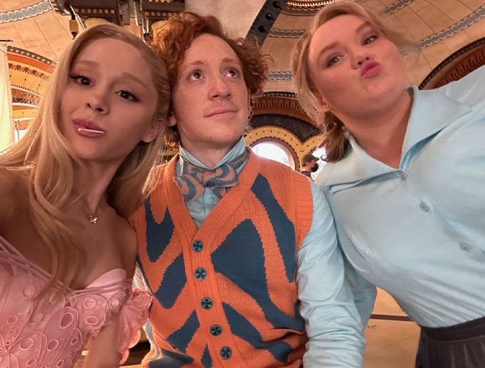 A trio posing in colorful outfits on a set, connected to Ariana Grande and Ethan Slater's "Wicked" romance. A trio posing in colorful outfits on a set, connected to Ariana Grande and Ethan Slater's "Wicked" romance.