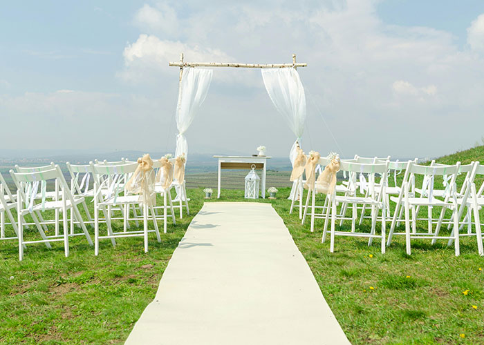 Outdoor wedding setup with white chairs and an aisle, featuring an arch adorned with sheer fabric, related to bridal event planning.