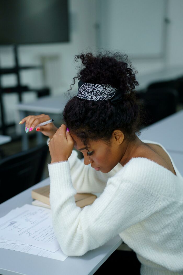 Babysitter studying notes at a desk, wearing a white sweater, and looking contemplative.