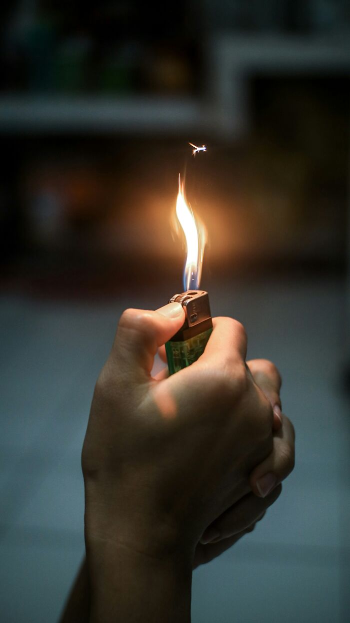 Hand holding a lit lighter, flames flickering in a dim setting.