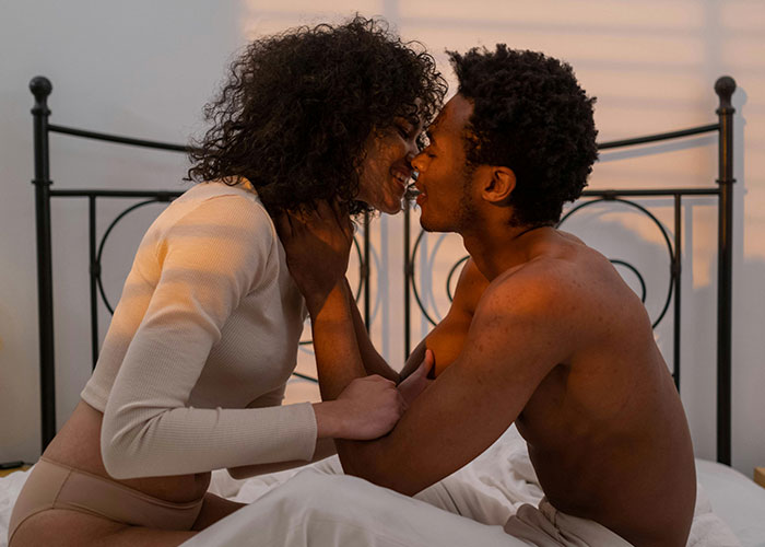 Couple sitting on a bed, intimately smiling at each other, highlighting relationship dynamics. Couple sitting on a bed, intimately smiling at each other, highlighting relationship dynamics.