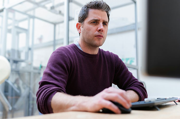 Man in purple sweater focused on computer screen, illustrating a life-altering decision.