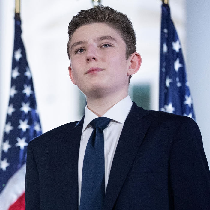 Young Trump in a suit standing in front of American flags, related to girlfriend rumors.