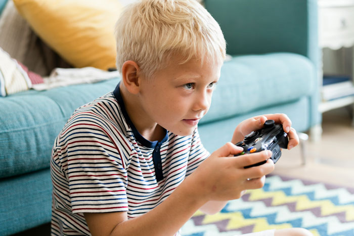 Child focused on playing a video game, holding a controller, sitting on a colorful carpet in a living room. Child focused on playing a video game, holding a controller, sitting on a colorful carpet in a living room.