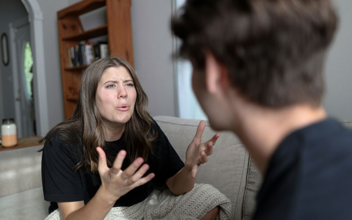 Woman on a couch gesturing emotionally at a man, discussing game skills. Woman on a couch gesturing emotionally at a man, discussing game skills.