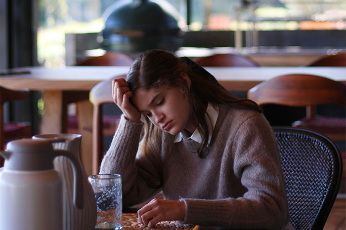 Young woman looking contemplative in a café, reflecting on biggest regrets from her 20s.