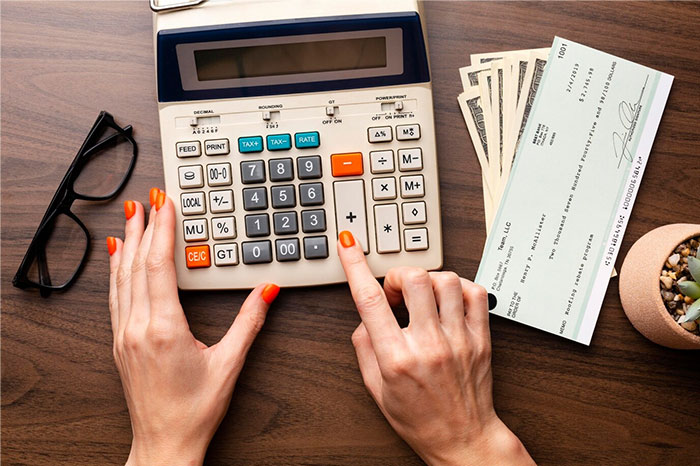 Hands with calculator and check, symbolizing financial regrets from people's 20s.