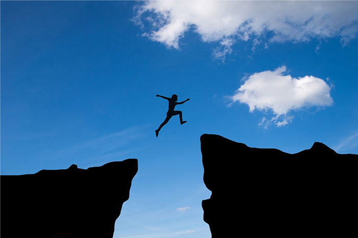 Person leaping across a large gap in a rocky landscape, symbolizing biggest regrets and taking risks in their 20s.