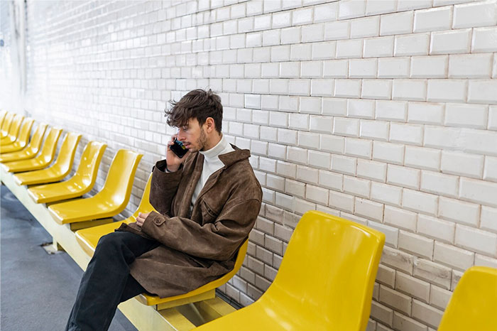Man sitting on yellow seats, talking on phone, reflecting on biggest regrets from twenties.