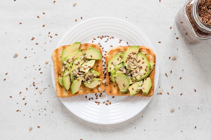 Avocado toast on a white plate with seeds, a common dietary choice often cited as a regret from people's 20s.