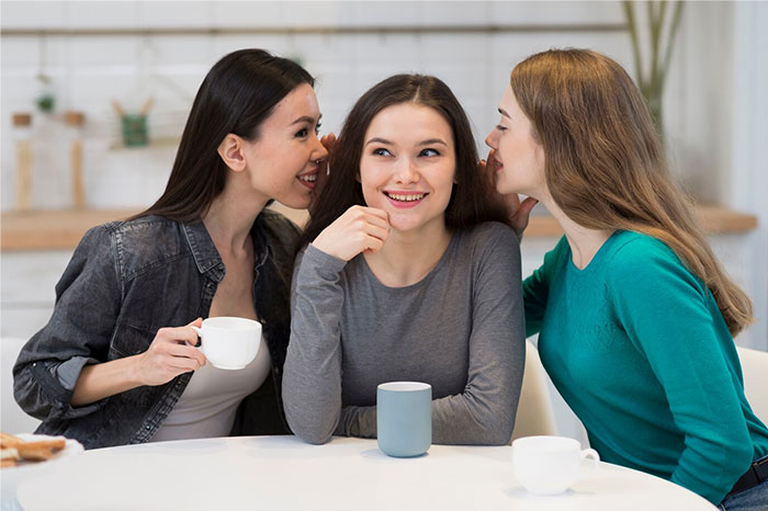 Three young women sharing secrets and drinking coffee, representing biggest regret discussions from people's 20s.