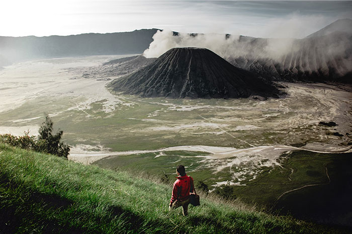 Person in red jacket overlooking scenic volcanic landscape, representing reflection on biggest regret from twenties.