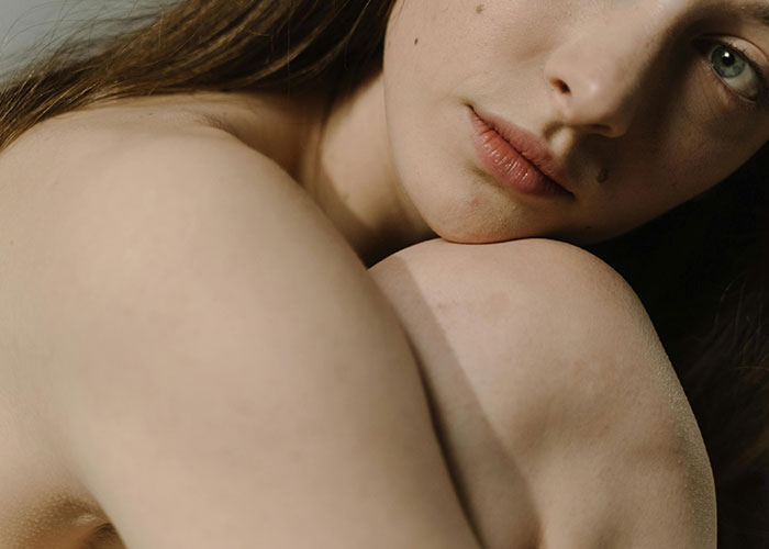 Close-up of a woman's face resting on her knee, conveying a thoughtful expression in a softly lit setting.