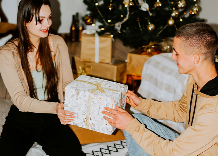 Couple exchanging gifts by the Christmas tree, featuring "mommy's boy" theme and sparking evident relationship tension.