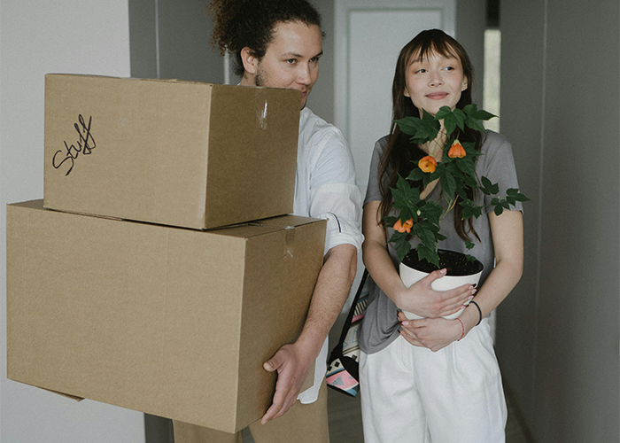 Couple moving into apartment, man carrying boxes, woman holding a plant, related to dog photo discussion. Couple moving into apartment, man carrying boxes, woman holding a plant, related to dog photo discussion.