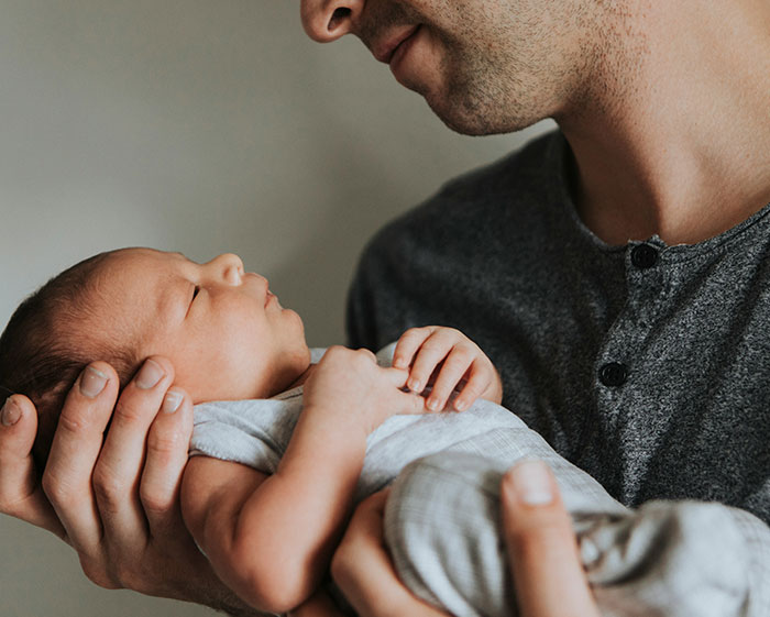 Father gently holding newborn baby, symbolizing breaking family tradition in naming practices. Father gently holding newborn baby, symbolizing breaking family tradition in naming practices.