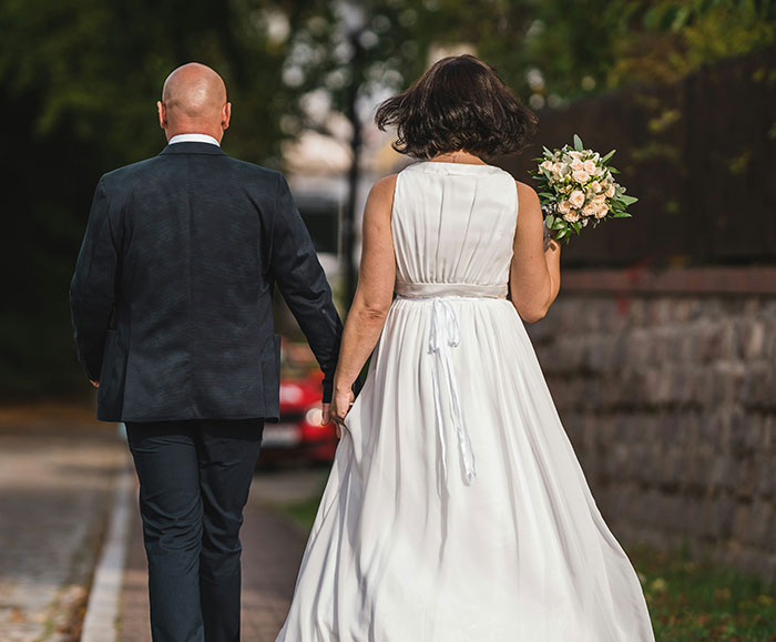 Bride and groom walking hand-in-hand outdoors, bride holding a bouquet, in a child-free wedding setting.