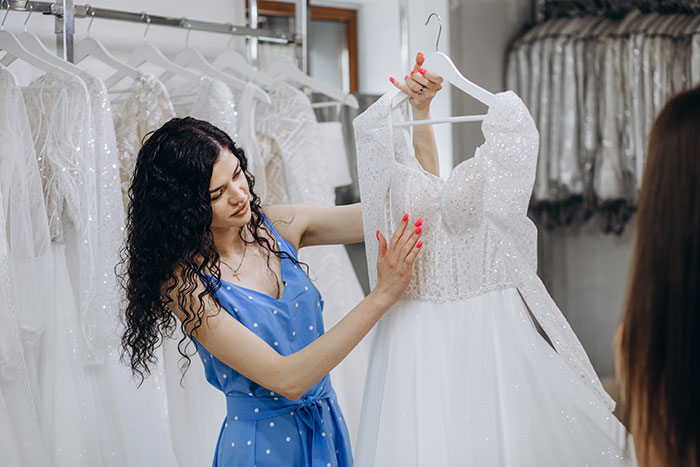 Woman examining a sparkly wedding dress in a boutique, showing her highlighted nails.