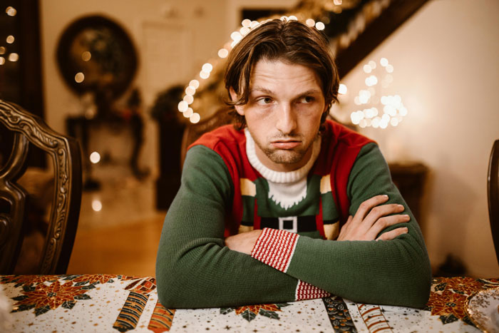 Man in a festive sweater looking pensive at a Christmas dinner table with holiday decorations in the background. Man in a festive sweater looking pensive at a Christmas dinner table with holiday decorations in the background.