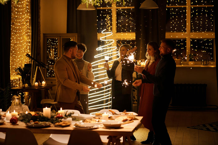 People celebrating Christmas with sparklers, festive lights, and a decorated dining table, creating a warm holiday atmosphere. People celebrating Christmas with sparklers, festive lights, and a decorated dining table, creating a warm holiday atmosphere.