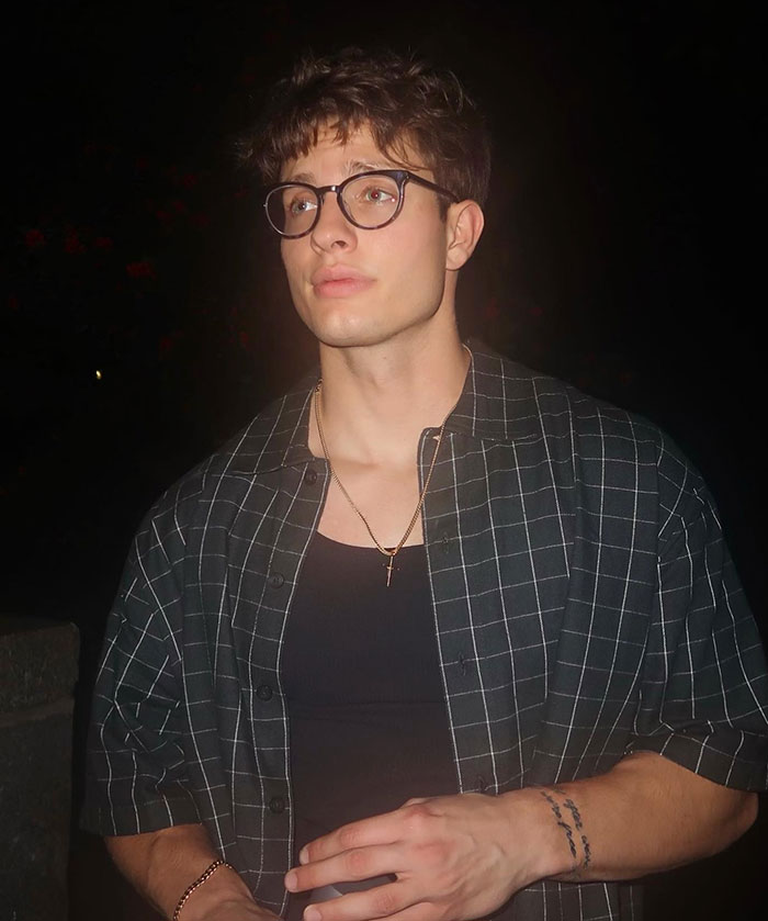 Matt Rife with a plaid shirt and glasses stands at night, before his changed appearance and dyed hair