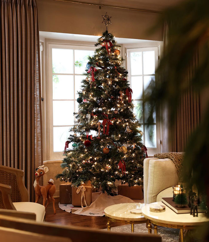 Elegant Christmas tree in a cozy living room, adorned with lights and ornaments, creating a festive ambiance.