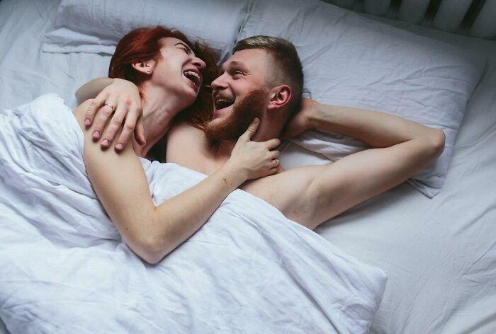 A couple laughing together in bed, exploring new habits after moving in.