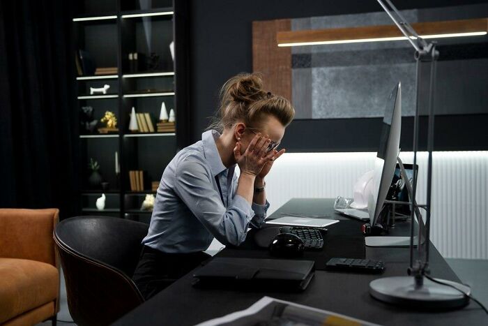 Employee at a desk, appearing stressed about receiving insulting benefits and bonuses, hands covering face.