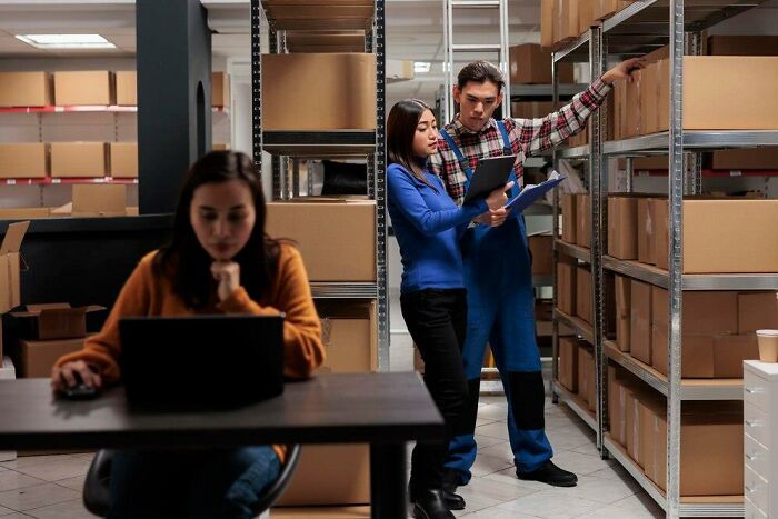 Workers in a warehouse discussing insulting benefits and bonuses, surrounded by shelves of boxes.