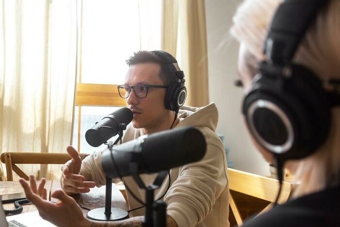 Two people recording a podcast, discussing insulting benefits and bonuses while wearing headphones and speaking into microphones.