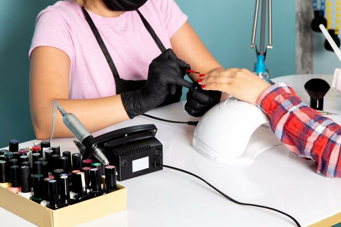 Manicurist with gloves applying red nail polish in a salon setting with various tools on the table.