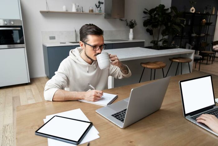Man drinking coffee, writing notes, and using a laptop in a modern kitchen setting for a discussion on controversial takes.