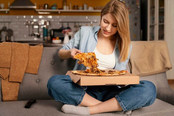 Woman enjoying pizza on a couch, illustrating a casual and relaxed moment.