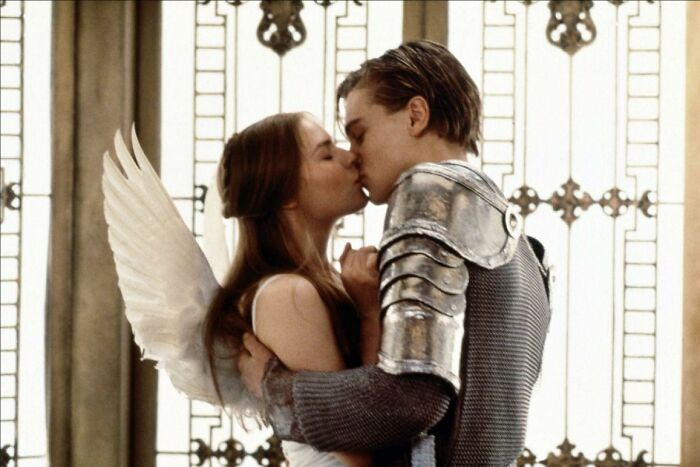 A romanticized couple kissing, with one wearing angel wings and the other in armor.