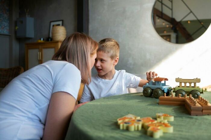 Mother and son whispering at a table with toy vehicles, illustrating romanticized family moments.