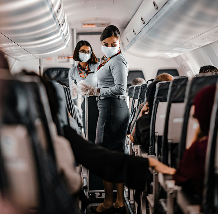 Flight attendants in an airplane aisle addressing passenger concerns about a seatmate's size.