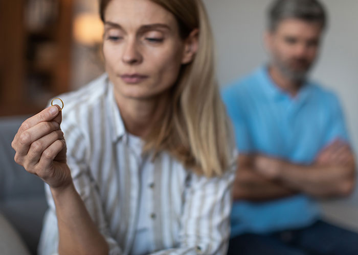 Woman holding a ring, man in background, reflecting on shocking comments about their partner.