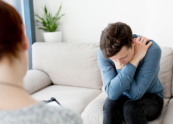 Man in a blue shirt sitting on a couch, appearing contemplative and troubled, highlighting relationship insights.