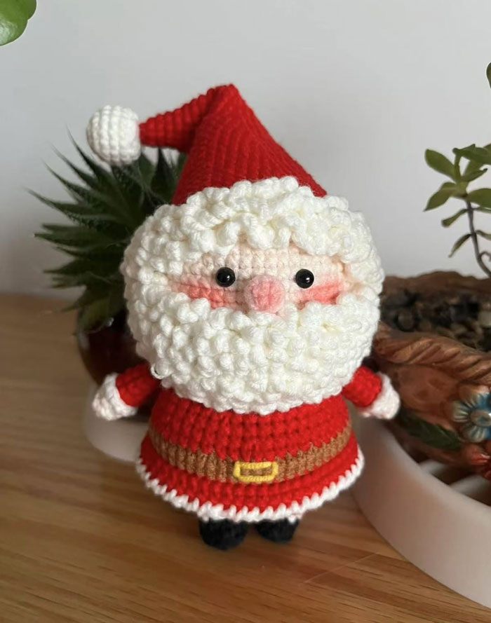 Crocheted Santa Claus toy as creative DIY Christmas decoration on a wooden table with plants.