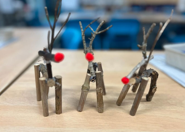 DIY Christmas decorations made from wooden sticks and red pom-poms, resembling reindeer on a wooden table.