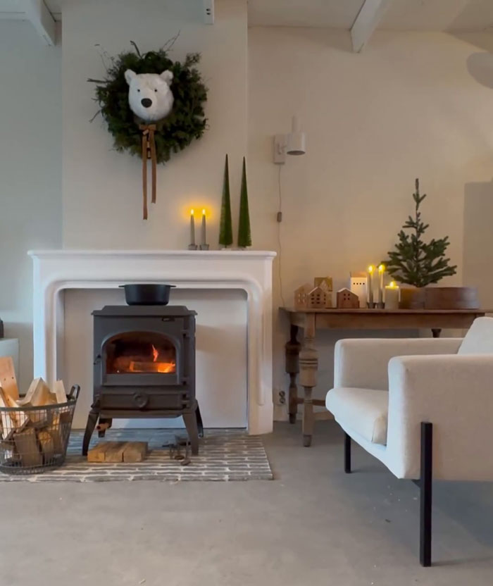 Cozy room with creative DIY Christmas decorations, featuring a bear wreath, candles, and a small tree by a warm fireplace.