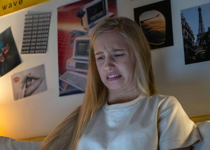 Teen girl looking shocked at her phone, related to texts from 60-year-old coach.