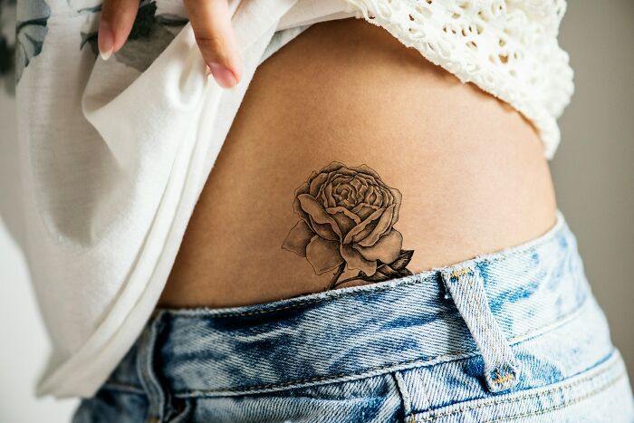 A rose tattoo on a person's hip, wearing a white shirt and blue jeans, showcasing body art style.