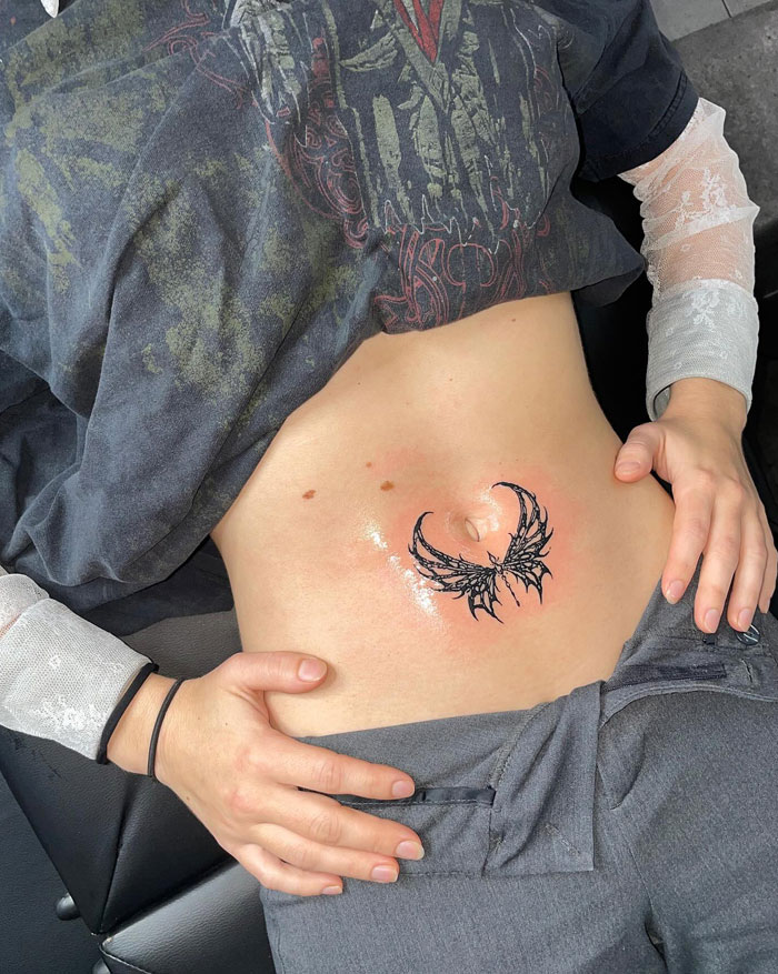 Tattoo featuring cybersigilism design on a person's abdomen, showcasing intricate black winged patterns.