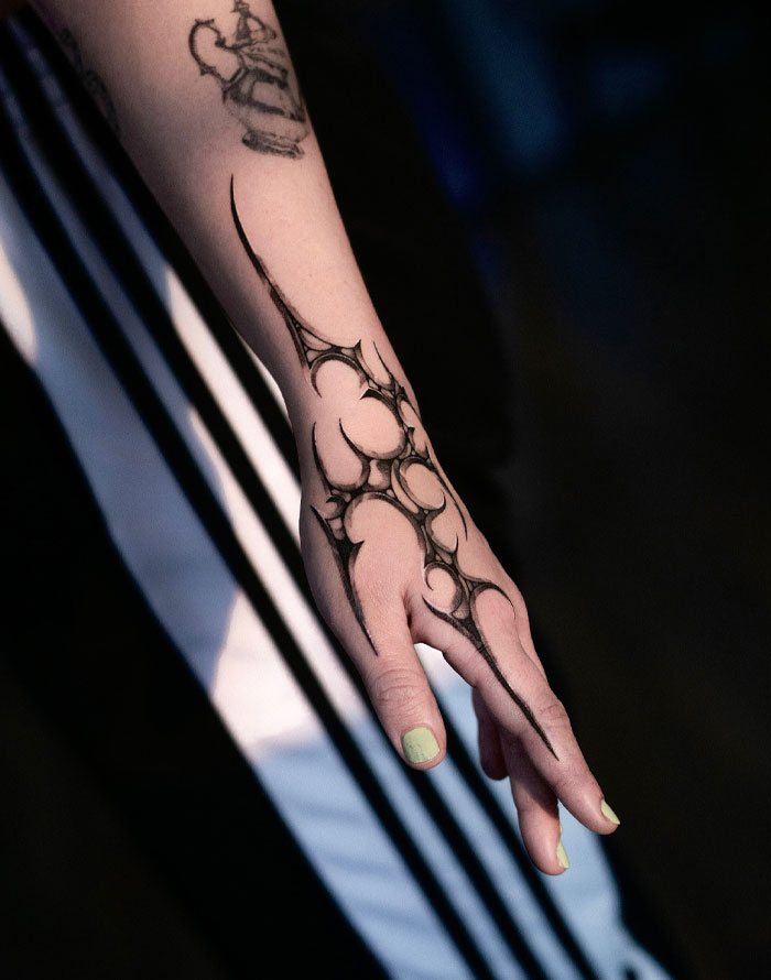 Tattoo on arm featuring intricate cybersigilism design with dark lines and abstract symbols.