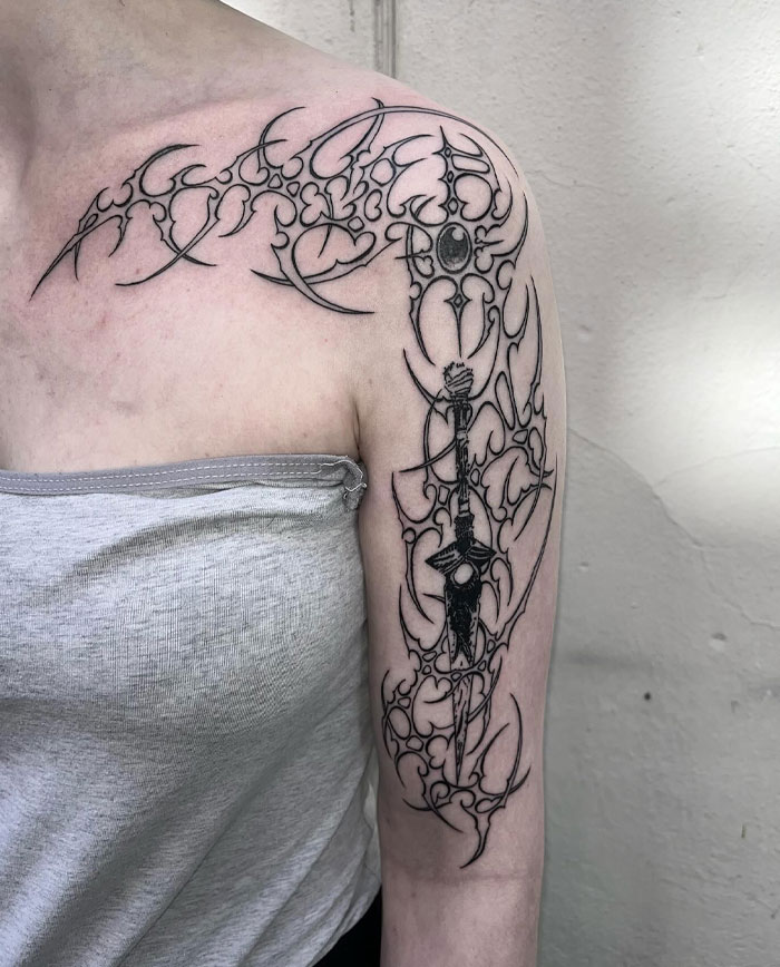 Stylized cybersigilism tattoo with intricate symbols on a person's upper arm in black ink.